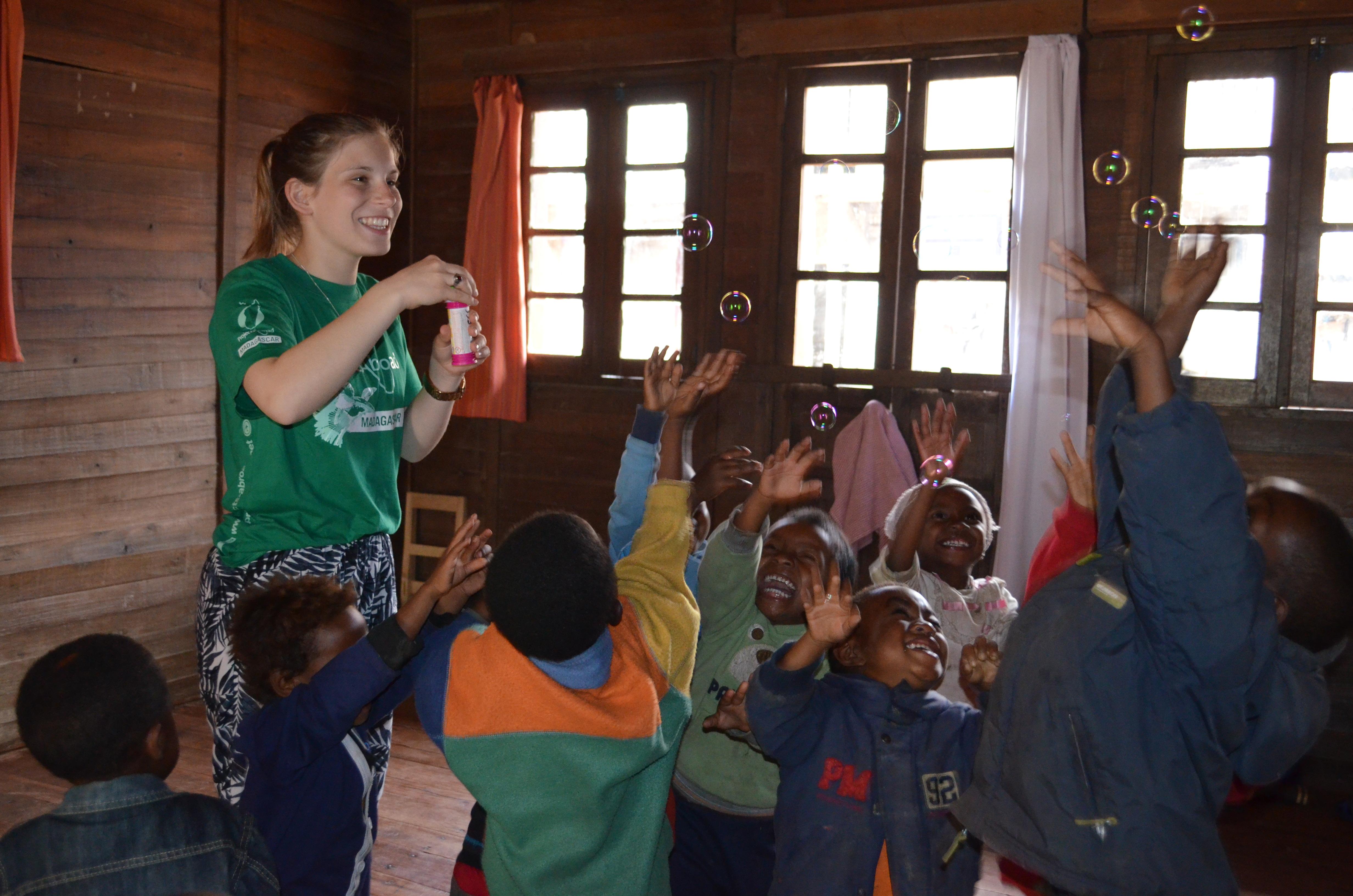 A female volunteer blows bubbles to a group of children trying to catch them during a kindergarten lesson at her Childcare Project in Madagascar. Projects Abroad volunteer with children in Madagascar blows bubbles for a group of children to catch at her Childcare placement.